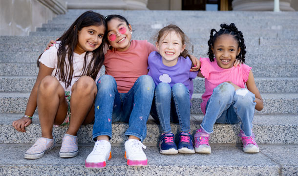 Four girls sitting with arms around each other smiling. Become a girl scout campaign