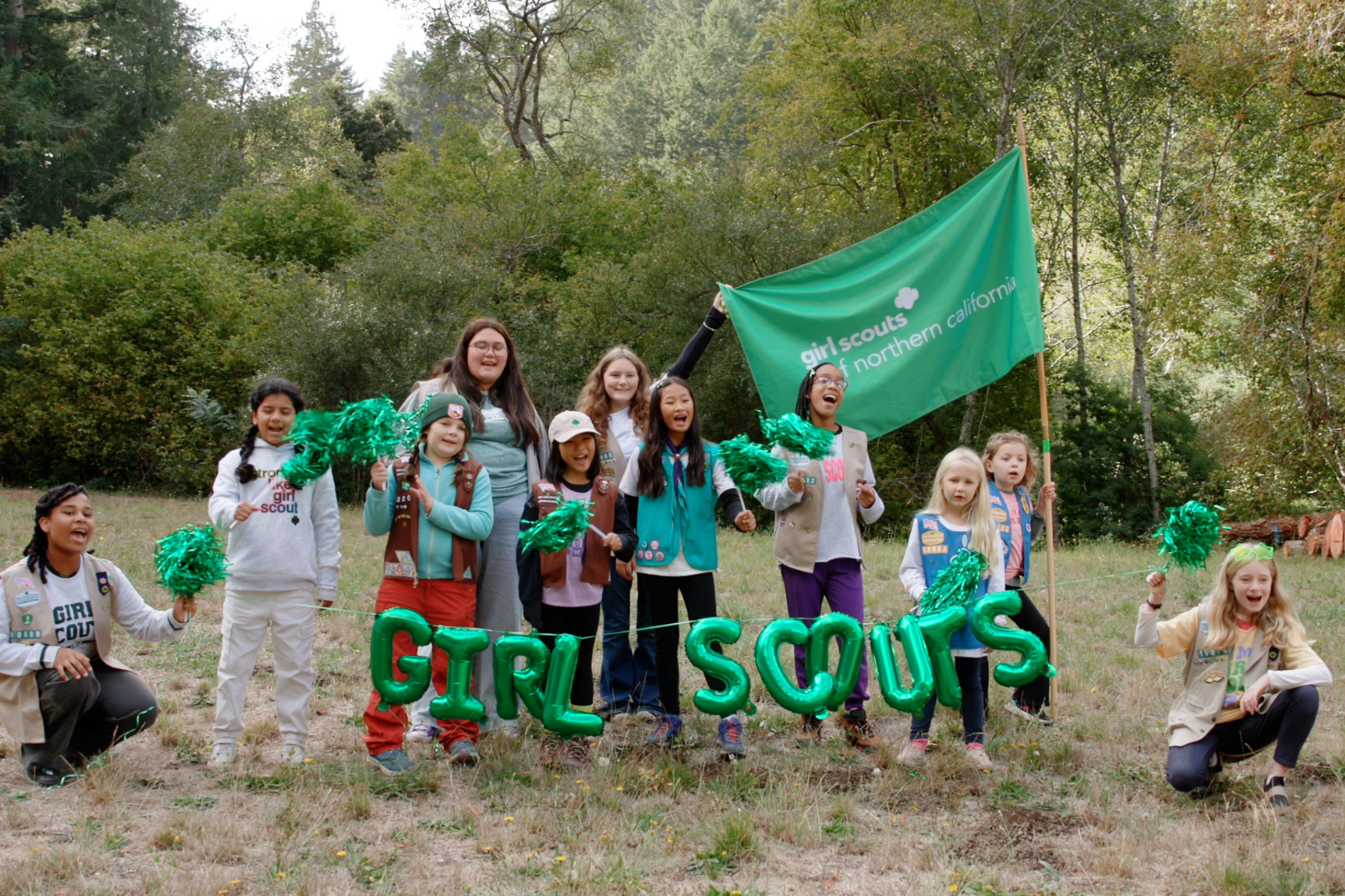 Girl scouts with green balloons that read 'girl scouts' sumiling and waving pompoms in a group 